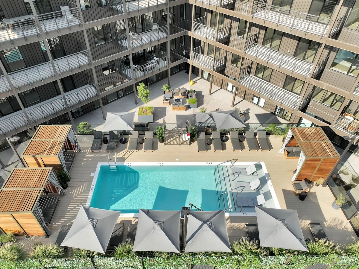 A sparkling swimming pool surrounded by comfortable lounge chairs and shaded areas, framed by lush landscaped greenery. The tranquil water reflects the sky, creating a relaxing and luxurious resort-like atmosphere perfect for unwinding or socializing outdoors.