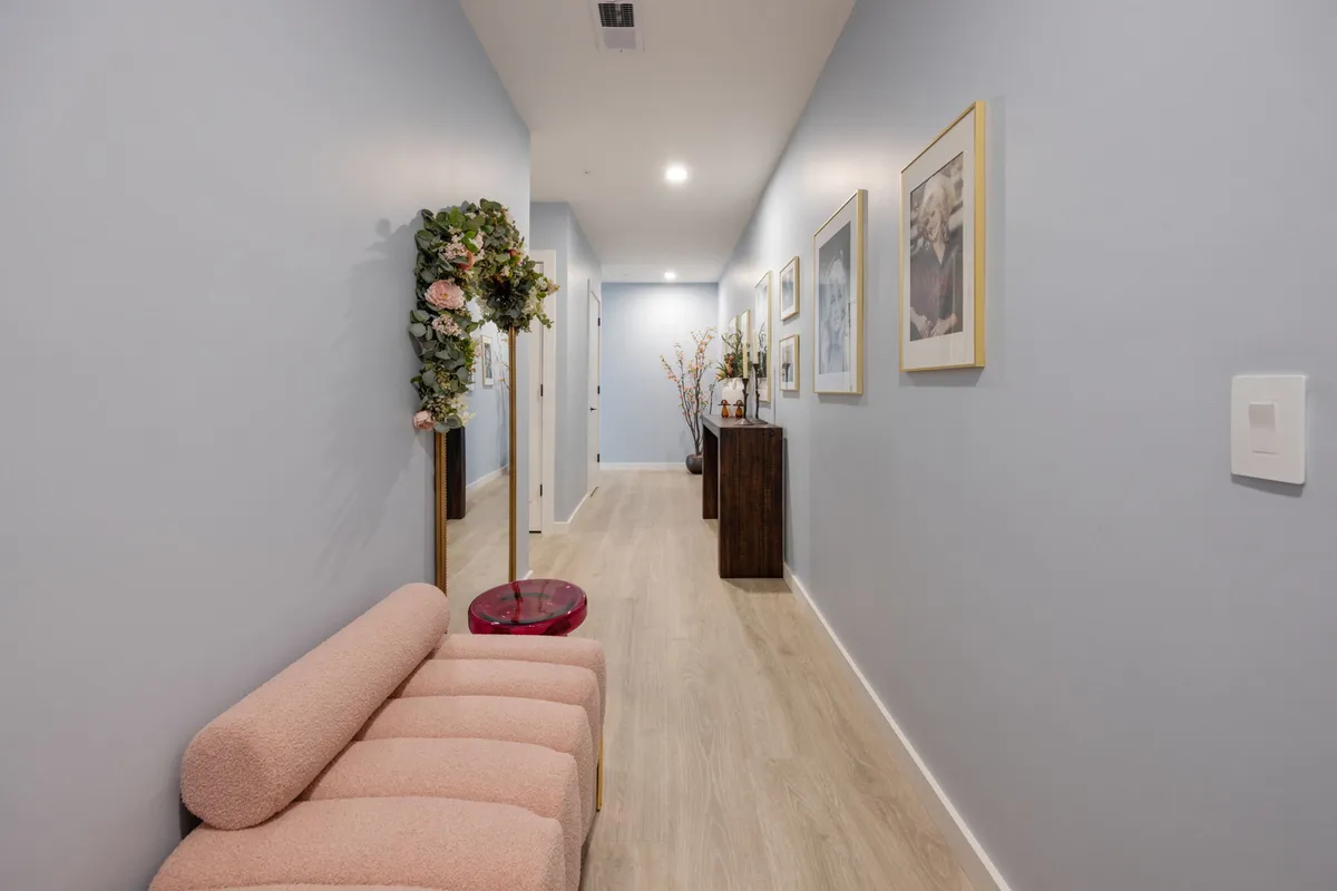 A bright, inviting living space featuring a playful pink sofa, a vibrant flower arrangement, a wooden cabinet, and framed artwork. The decor is bold yet warm, blending a modern touch with a sense of personality that could fit a Dolly Parton-themed interior.