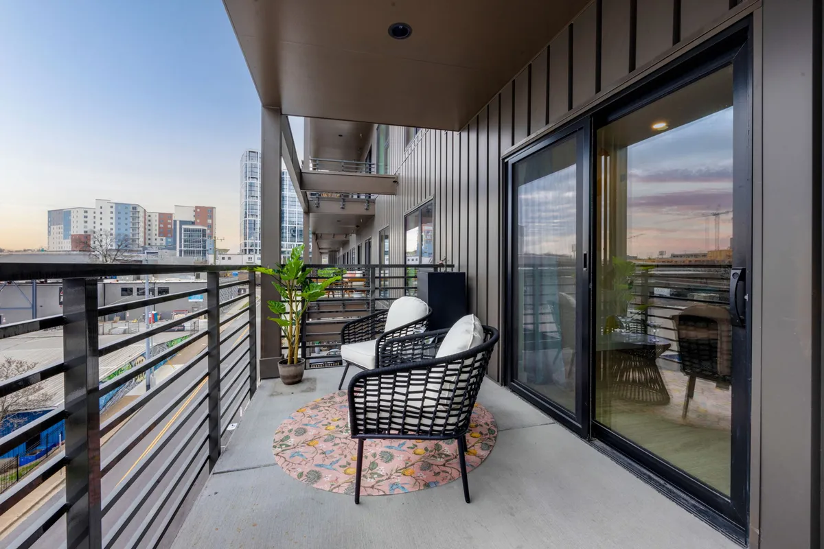 A cozy balcony with comfortable seating, decorative rug, potted plant, and a view of the city. The inviting setup suggests relaxing after a day out, enjoying city views, and reflecting on the day’s musical adventures.