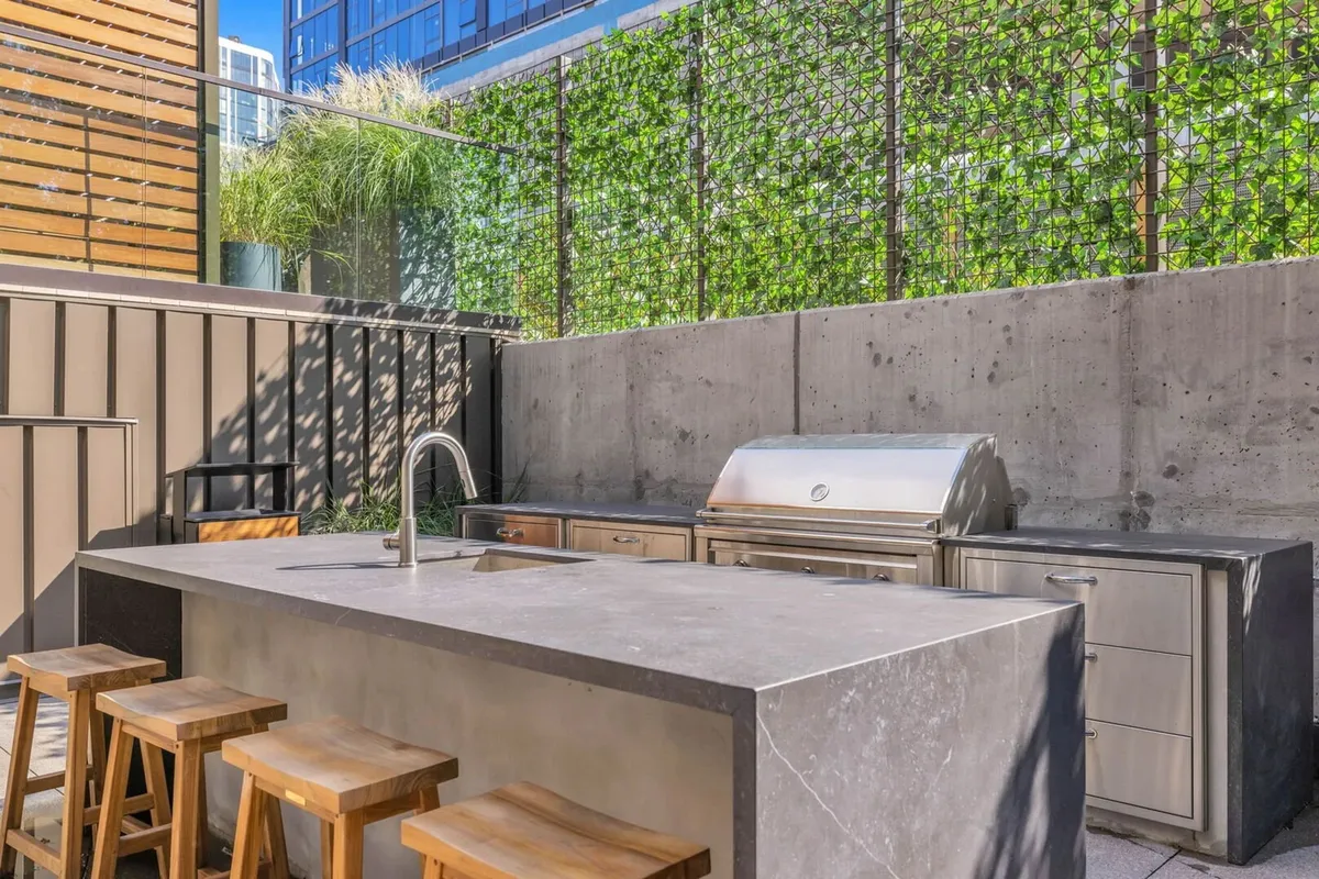 A modern outdoor kitchen and BBQ area with a grill, island seating, and a lush green wall backdrop. The space is tailored for social gatherings, alfresco dining, and community barbecues.