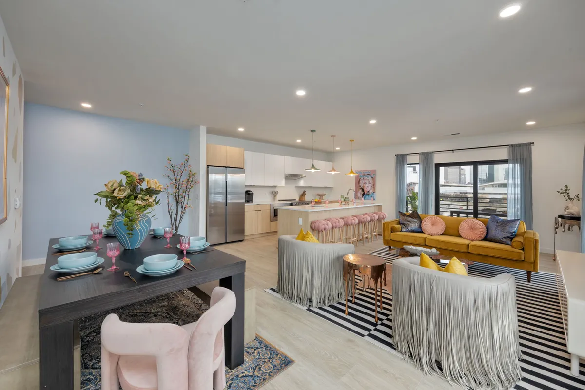 An inviting dining area set with a floral centerpiece, adjacent to a yellow sofa and kitchen island. The striped rug and contemporary decor create a cheerful, celebratory mood, making this space ideal for dining, socializing, and group events.